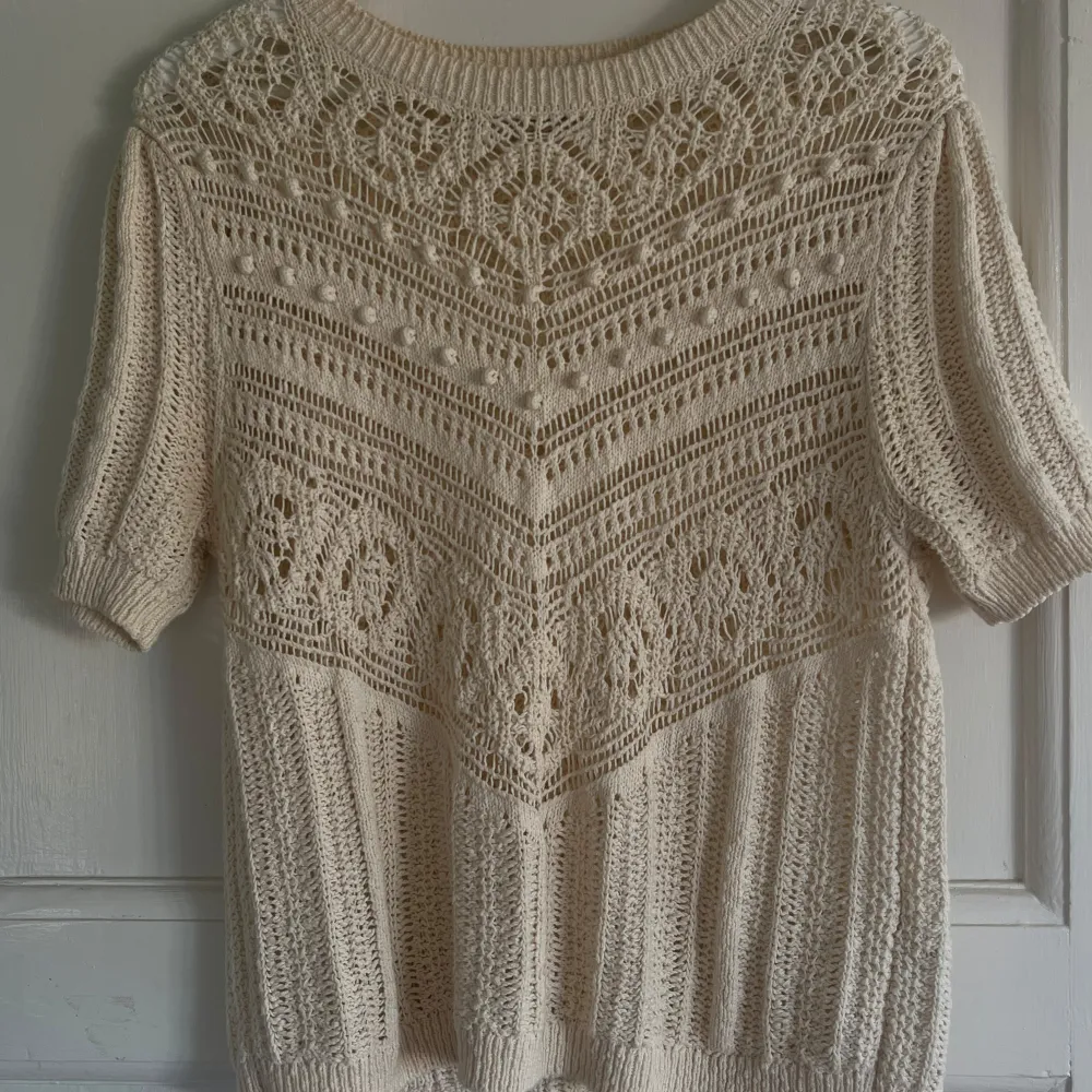 Säljer en vacker vit/beige stickad topp med korta ärmar och ett detaljerat mönster. Perfekt för en stilren och elegant look. . T-paidat.