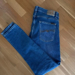 Blå jeans från Nudie Jeans - Snygga blå jeans från Nudie Jeans med klassisk femficksdesign och broderade bakfickor. De har en normal passform och är perfekta för en avslappnad stil. Tillverkade i slitstarkt denim. Storlek W33 L32