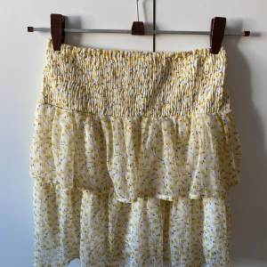 Gul blommig kjol från Vero Moda - Charmig gul kjol från Vero Moda med blommigt mönster. Kjolen har en smockad midja och volangdetaljer som ger en luftig och somrig känsla. Perfekt för varma dagar!🩷