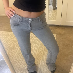 Grå jeansbyxor - Snygga grå jeansbyxor med låg midja och knappstängning. Byxorna har en klassisk femficksdesign och en rak passform som ger en avslappnad look. Perfekta för en casual stil.