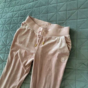 Rosa juicy byxor - Snygga och bekväma rosa mjukisbyxor med snörning i midjan och gulddetaljer på snörena. Byxorna har en broderad juicy catoure logga på sidan.