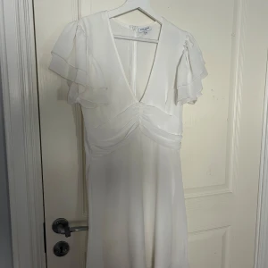 Vit klänning från Bubbelroom - Vit klänning från Bubbelroom med v-ringning och volangdetaljer på ärmarna. 
