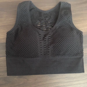 Svart nätmönstrad sporttopp - Säljer en svart sporttopp med nätmönster och breda axelband. Toppen har en tight passform och är perfekt för träning. Materialet är stretchigt och andas bra. Passar utmärkt för en aktiv livsstil. Använd några fåtals gånger