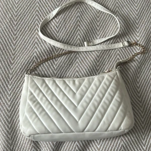 Vit quiltad axelväska - Snygg vit axelväska med quiltat mönster och guldkedja. Perfekt för att ge en elegant touch till din outfit. Väskan har en justerbar axelrem för bekväm passform. Pris går att diskutera
