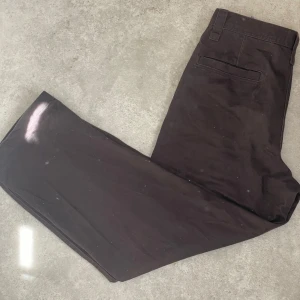 Bruna kostymbyxor från Uniqlo - Snygga bruna kostymbyxor med baggy passform. De har en klassisk design med hällor för bälte och en knappstängning framtill. Perfekta för en stilren look.