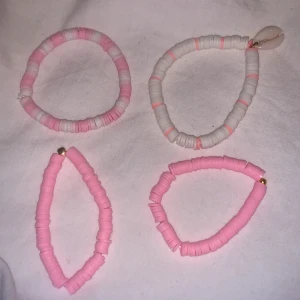 Färgglada armband i rosa och vitt - Fyra elastiska armband i rosa och vitt med claybead runda pärlor. Ett av armbanden har en dekorativ snäcka och två andra har en liten guldfärgad pärla. Perfekt för att lägga till en färgglad touch till din stil. De kostar 25st