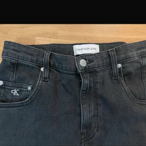 Svarta jeans från Calvin Klein - Snygga svarta jeans från Calvin Klein med klassisk femficksdesign och logotypdetaljer på fickan och bak. De har en knappgylf och är perfekta för en stilren look. 