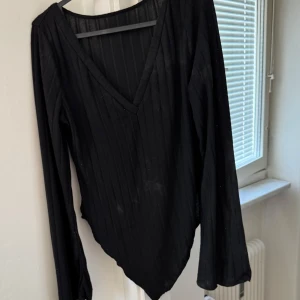 Svart ribbad långärmad topp - Säljer en stilren svart ribbad topp med v-ringning och långa ärmar. Perfekt för en elegant och enkel look. Passar bra till både jeans och kjol. Toppen är smutsad osäker om fläckar går bort i tvätt.