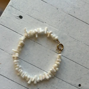 Vitt pärlarmband från Edblad - Elegant vitt armband från Edblad med oregelbundna pärlor och en guldig låsdetalj. Perfekt för att lägga till en touch av stil till din outfit.