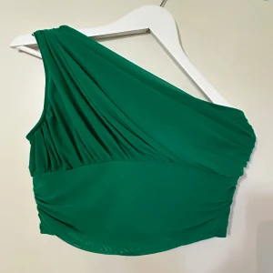 Grön oneshoulder topp - Snygg grön oneshoulder topp med draperad design. Perfekt för en stilren och modern look. Passar bra till både jeans och kjol. Aldrig använd 