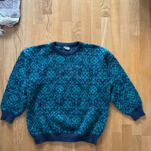 Blå och turkos mönstrad tröja från Elisa - Säljer en snygg blå och turkos tröja från Elisa med ett unikt mönster. Tröjan är stickad och har långa ärmar samt ribbade muddar vid ärmslut och nederkant. Perfekt för kyligare dagar!