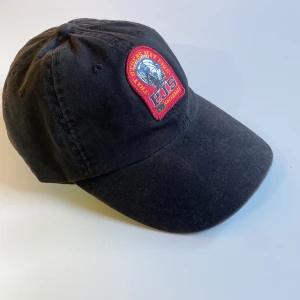 Parajumper keps - Snygg svart parajumper keps med en broderad patch framtill. Kepsen har en justerbar rem baktill för perfekt passform. Endast använd några få ggr. Perfekt för sommarens avslappnade stil. Strl: OneSize  Skick 8/10