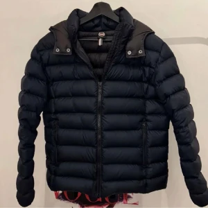 Blå jacka från Colmar - Snygg svart dunjacka från Colmar med dragkedja och hög krage. Perfekt för kyliga dagar med sin vadderade design. Jackan har långa ärmar och en stilren look. Passar mellan 175-184 cm