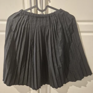 Svart plisserad kjol från Dreams - Svart kort plisserad kjol från Dreams med elastisk midja. Kjolen har en klassisk och stilren look med tydliga veck som ger extra volym och rörelse. Perfekt för dig som gillar en enkel men snygg stil.