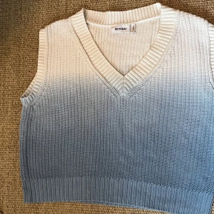 Stickad väst i ombre från Weekday - Säljer en stickad väst från Weekday med snygg ombre-effekt i vitt och grått. Västen har v-ringning och bred ribbad kant vid hals och ärmhål. Perfekt att styla över en skjorta eller t-shirt för en trendig lager-på-lager-look.