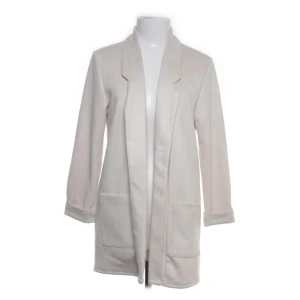 Beige cardigan jacka från Amesw - Lång, beige cardigan jacka från Amisu  med klassisk krage och två stora fickor framtill. Jackan är tillverkad i mjuk polyesterblandning och har långa ärmar med uppvikta muddar. Perfekt för lager-på-lager och chill vibes.