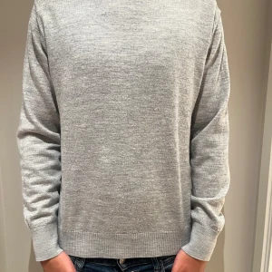 Grå stickad tröja från Bruun & Stengade - En stilren grå stickad tröja med rund hals och ribbade muddar vid ärmslut och nederkant. Tröjan har en klassisk passform och är perfekt för lager-på-lager. Enkel att matcha med jeans eller andra byxor för en clean look. Jätte bra skick, passar S/M