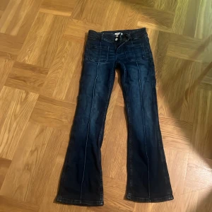 Mörkblå bootcut jeans Gina Tricot - Snygga mörkblå jeans från Gina Tricot i bootcut-modell. Jeansen har hög midja, framfickor med markerade sömmar och dubbla knappar i midjan. Tillverkade i stretchig denim för en bekväm passform.