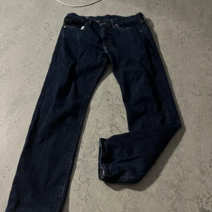 Levi's 501 mörkblå jeans - Klassiska Levi's 501 jeans i mörkblå denim med raka ben och femficksmodell. Byxorna har den ikoniska läderpatchen bak i midjan och synliga kontrastsömmar. Perfekta för dig som gillar tidlös stil och vill ha ett par jeans som funkar till allt. Storlek w31 L30