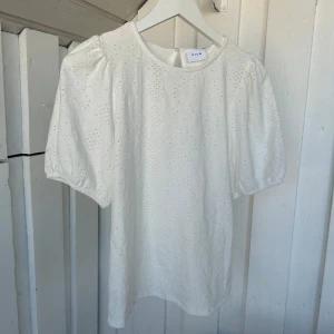 Vit blus med puffärm från Vila XS - Superfin vit blus från Vila i storlek XS med broderade detaljer och puffiga 2/4-ärmar. Blusen har rund halsringning och en liten knapp i nacken. Perfekt för en fräsch och somrig look!