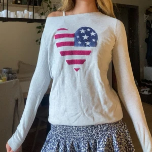 Ljusgrå stickad tröja Tommy Hilfiger - Snygg ljusgrå stickad tröja från Tommy Hilfiger med ett stort hjärta på bröstet i amerikanska flaggans färger🇺🇸. Tröjan har lång ärm, bred halsringning och ribbade muddar. Perfekt för dig som gillar casual och cool stil. Fin till allt👌🏼🤩
