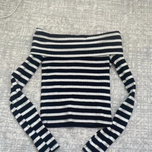 Randig offshoulder topp i ribbad bomull - HELT NY Snygg svartvit randig offshoulder topp med långa ärmar. Ribbad struktur som ger en tight och skön passform. Perfekt för dig som gillar en trendig och stilren look. Gjord i mjuk bomull som känns bekväm hela dagen.