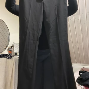 Svarta vida kostymbyxor - Säljer ett par svarta kostymbyxor med vida ben och klassiska bakfickor. Byxorna har hällor för bälte och är i ett stilrent snitt som ger en clean look. Perfekta om du gillar en loose och relaxed vibe.tvättas vid försäljning 