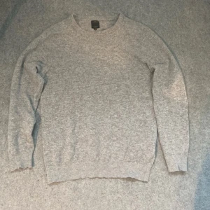 Grå stickad tröja från Daniel Dodd - Säljer en enkel och stilren grå stickad tröja från Doppelgänger i storlek M. Tröjan har rund hals, långa ärmar och ribbade muddar vid ärmslut och nederkant. Perfekt för dig som gillar en clean look och vill ha något mjukt och bekvämt till hösten och vintern.