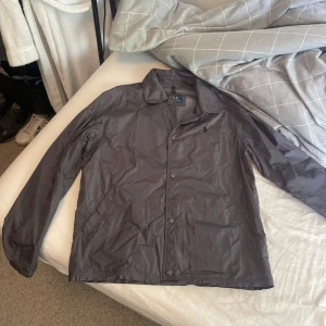 Ralph Lauren höstjacka  - Svart vindjacka från Polo Ralph Lauren Snygg och lätt jacka i tunnare material, perfekt för vår och höst. Klassisk design med krage, tryckknappar framtill och två sidfickor. Liten broderad Polo-logga på bröstet. Storlek: S Skick: Mycket bra – inga fläckar eller skador, endast lite skrynklig efter förvaring. 