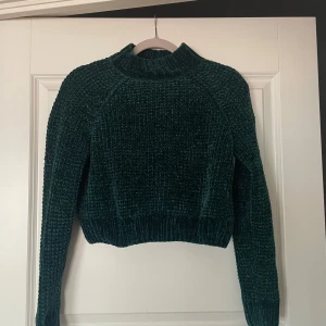 Mörkgrön stickad tröja Divided H&M - En oanvänd Mysig mörkgrön stickad tröja från Divided H&M med lite hög krage och lång ärm. Tröjan har en snygg struktur och är lite croppad i modellen, perfekt nu till hösten. Materialet är mjukt och ger en skön, avslappnad vibe.