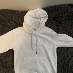 Vit hoodie  - Snygg vit hoodie från C med broderad CD-logga på bröstet. Klassisk känguruficka, dragsko i huvan och mjukt material som känns riktigt lyxigt. Perfekt för dig som vill ha en clean och stilren look.