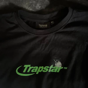 Svart Trapstar t-shirt - Svart t-shirt från Trapstar med grönt logotryck och radar-inspirerat motiv både fram och bak. Klassisk rund hals och avslappnad passform. 