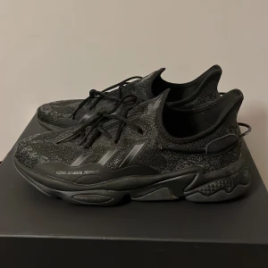 Svarta Adidas Ozweego sneakers - Snygga svarta Adidas Ozweego sneakers med stickad ovandel och chunky sula. Skorna har diskreta reflexdetaljer, klassiska tre ränder på sidan och snörning framtill. Perfekta för dig som gillar en sportig och modern look. Använda en gång.