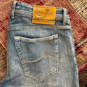 Jacob Cohën limited edition - Snygga ljusblå jeans från Jacob Cohën med klassisk femficksdesign och guldfärgad patch bak. Jeansen har raka ben, diskret slitning och kontrastsömmar. Perfekta för dig som gillar stilrena och bekväma jeans med exklusiv känsla. Väldigt snygg tvätt och snygga detaljer. Säljer pågrund av behov av pengar. Skick 9/10. Str 34 och sitter typ som vanliga 34 or. Byxorna är limited edition och är som nya. Pris kan diskuteras vid snabb affär!