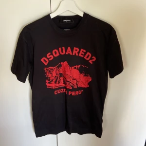 Svart Dsquared2 t-shirt med röd print - Cool svart t-shirt från Dsquared2 med röd grafik och texten 'Cuzco Peru' på bröstet. Klassisk passform med rund hals och korta ärmar. Perfekt för dig som gillar streetwear och vill sticka ut med en snygg printad tee.