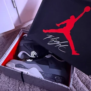 Nike Jordan 4 sneakers grå och svart Skorlek 45/46 - Nike Jordan 4 sneakers i grå och svart med vita detaljer och specklad sula. Skorna har meshpaneler, snörning och en chunky siluett som ger en riktigt cool vibe. Perfekt för dig som vill sticka ut med klassiska och stilrena sneakers.