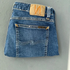 Blåa Nudie Jeans - Snygga blå jeans från Nudie Jeans. När du köper dessa jeans får du 110 exklusiva leverantörer där du hittar jeans som dessa för 40kr gratis. Jeansen har en slim passform. Nypris 1600kr mitt pris 349, Helt ny och inga defekter/hål eller fläckar. 
