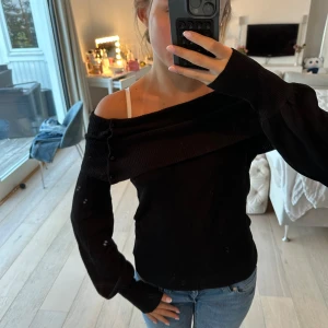 Svart offshoulder stickad tröja  - Svart stickad offshoulder-tröja från Ted Baker med snygga knappar längs den breda kragen. Tröjan har lång ärm och sitter snyggt med en lite tightare passform. Vintage från 00-talet. 