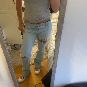 Ljusblå slitna bootcut jeans  - Säljer ett par ljusblå jeans med bootcut passform och snygga slitningar över knäna och bakfickan. 