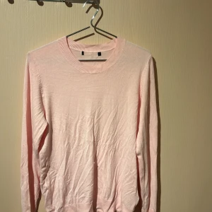 Ljusrosa stickad tröja - En enkel och stilren ljusrosa stickad tröja med rund halsringning och långa ärmar. Tröjan har en mjuk känsla och ribbade muddar vid hals, ärmslut och nederkant. Perfekt för lager-på-lager och passar till många olika outfits. Klippt bort lappen för nån vecka sen för den va ivägen! Men äe från lager och i storlek S