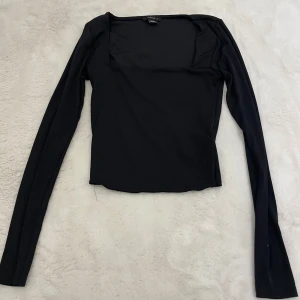 Svart långärmad topp från New Yorker - En svart långärmad topp från New Yorker med fyrkantig urringning. Toppens passform är slim och den är tillverkad i ett mjukt, stretchigt material som känns skönt mot huden. Perfekt att styla med jeans eller kjol för en clean look.