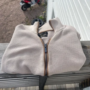  Massimo Dutti tröja - Snygg beige kofta från Massimo Dutti i extrafin bomull. Tröjan har en grovstickad struktur, hög krage och detaljerad dragkedja med bruna kanter. Perfekt för dig som gillar stilrena och klassiska plagg med modern touch.