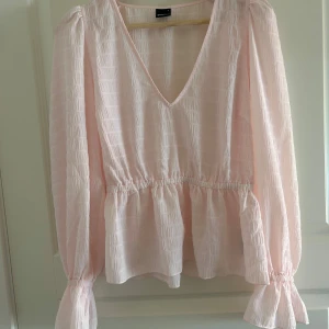Ljusrosa blus med volangärm - Supersöt ljusrosa blus från Gina Tricot med v-ringning, markerad midja och volangiga långa ärmar.