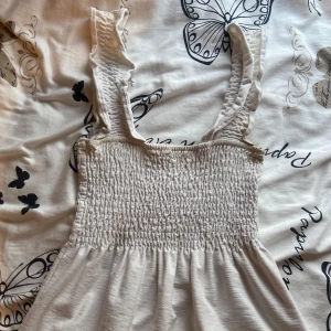 Vit topp med volanger ned till från H&M - Säljer denna vita topp med volanger ned till från h&m i storlek M men upplevs dock mer som en S och har ett stretchigt material 