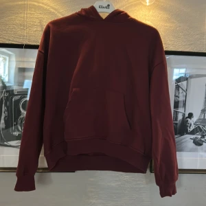 Vinröd hoodie från 157, storlek S - Mysig vinröd hoodie från 157 i storlek S. Klassisk modell med huva och stor magficka framtill. Tröjan har ribbade muddar vid ärmslut och nederkant. Perfekt för chill dagar eller när du vill ha en enkel och snygg look.