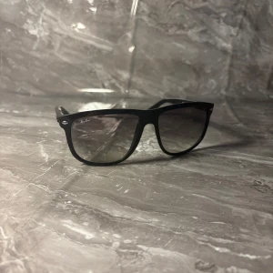 Rayban boyfreind  - Snygga svarta Ray-Ban solglasögon i klassisk Wayfarer-modell. Bågarna är i blank plast och har mörka tonade glas. Diskret Ray-Ban-logga på skalmen och framtill. Perfekta för en cool och tidlös stil.