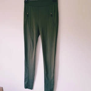 Olivgröna slim leggings med detalj dragkedjor från bikbok strl M - Snygga olivgröna leggings med slim fit och coola dragkedjor vid fickorna framtill. Byxorna har hög midja och är tillverkade i ett stretchigt material som sitter tajt och bekvämt. Perfekta för en stilren och trendig look.  Detalj fickor Trådsläpp & tvättludd men inga hål och annars fint skick