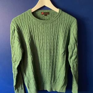 Grön stickad tröja från Dressmann - Snygg grön kabelstickad tröja från Dressmann i storlek M. Tröjan har rund halsringning, ribbade muddar och lång ärm. Perfekt för lager-på-lager och passar till både jeans och chinos. Enkel att matcha och superbekväm för kyligare dagar.