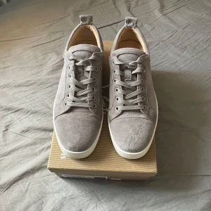 Grå mocka sneakers från Louboutin - Snygga sneakers från Christian Louboutin i ljusgrå mocka med röda sulor.skorna är i bra skick kanske en snabbt tvätt på sulorna så blir de som nya. Skriv vid funderingar 