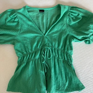 Grön blus med puffärm från Gina Tricot - Supersöt grön blus från Gina Tricot med puffiga korta ärmar och v-ringning . Toppen har en lätt strukturerad yta och markerad midja som ger en snygg siluett.